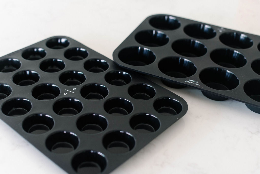 Two black muffin tins on a white surface