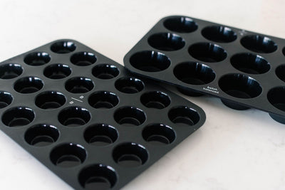 Two black muffin tins on a white surface
